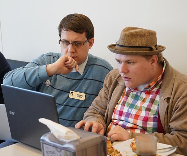 Two men sit side-by-side looking at a laptop. The man on the left has a nametag that reads, "Michael Barera" with the U T A Libraries logo.