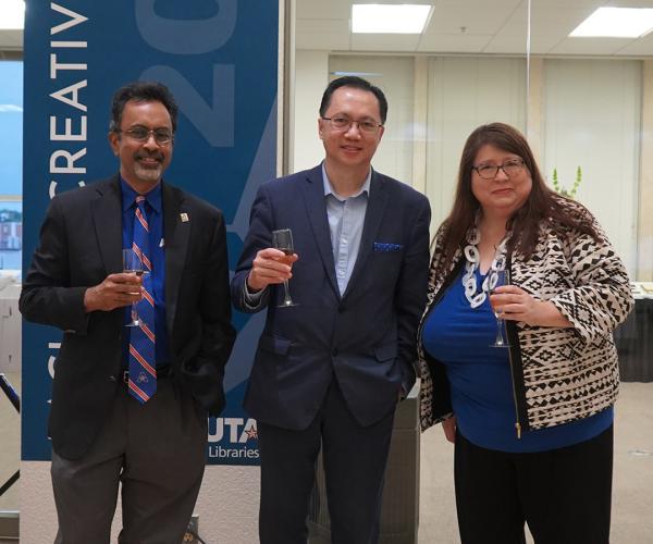 Provost Pranesh Aswath, President Teik Lim, and Dean Rebecca Bichel raise a glass of champagne in front of a Faculty Creative Works banner in Central Library.