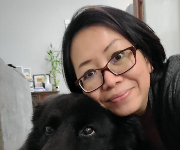 A woman wearing glasses poses with a black dog for a selfie.