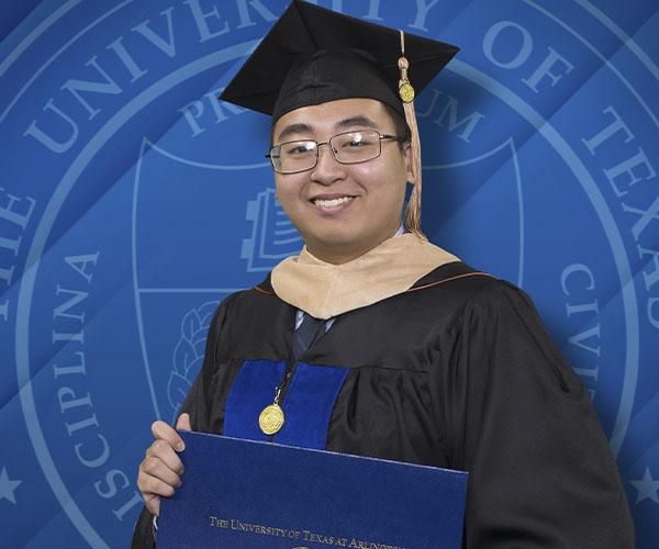 Kevin Huynh in his graduation gown holding his degree certificate, standing in front of UTA seal blue and white background.